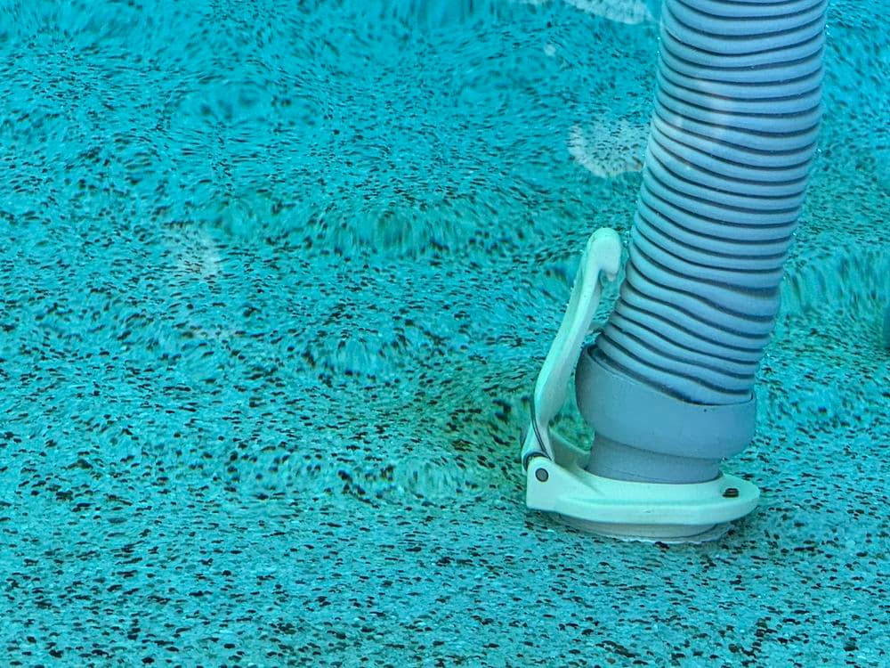 Close-up of a pool vacuum hose submerged in clear blue water with a textured pool bottom.