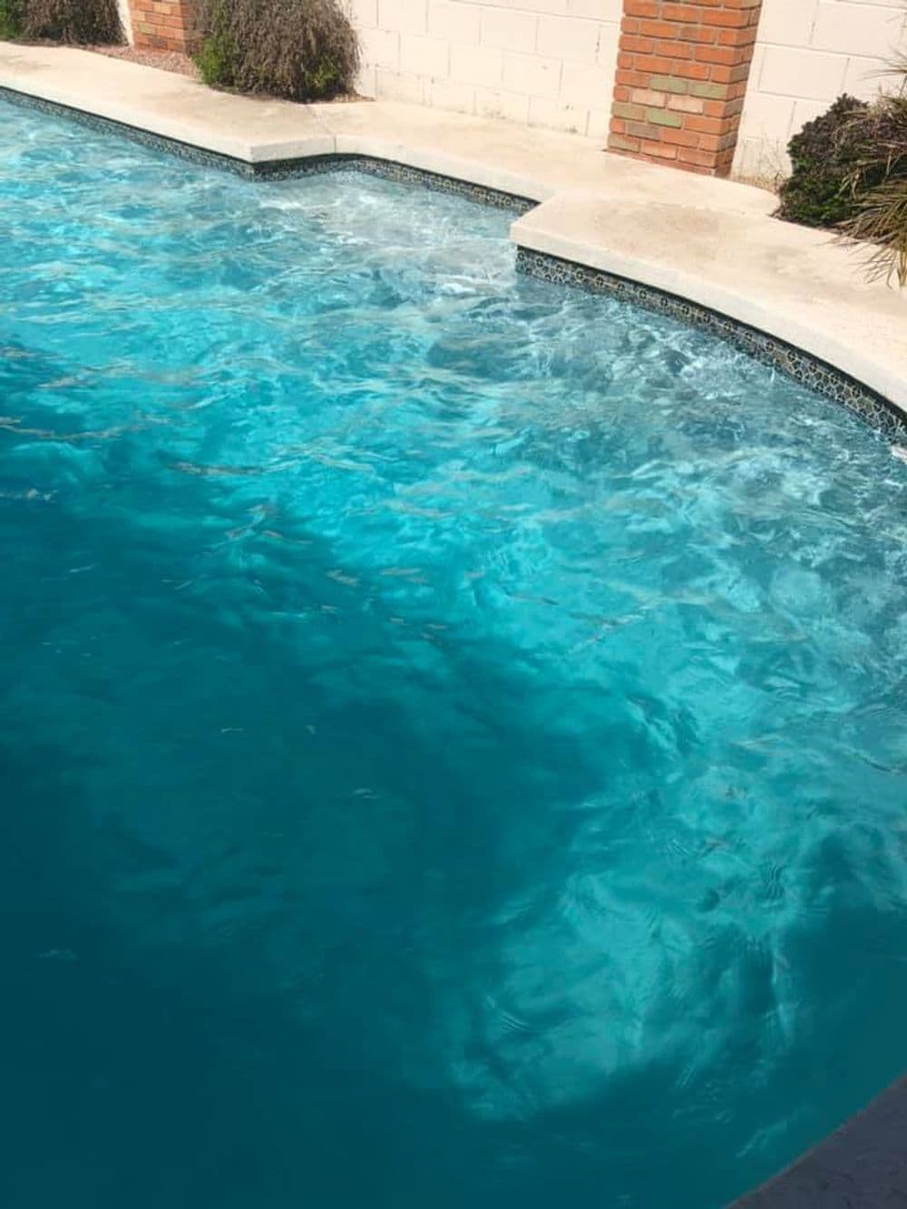 Vibrant blue swimming pool water with gentle waves and concrete edge design.