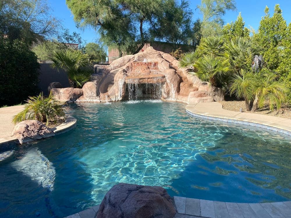 Backyard oasis featuring a rock waterfall, palm trees, and clear blue swimming pool.