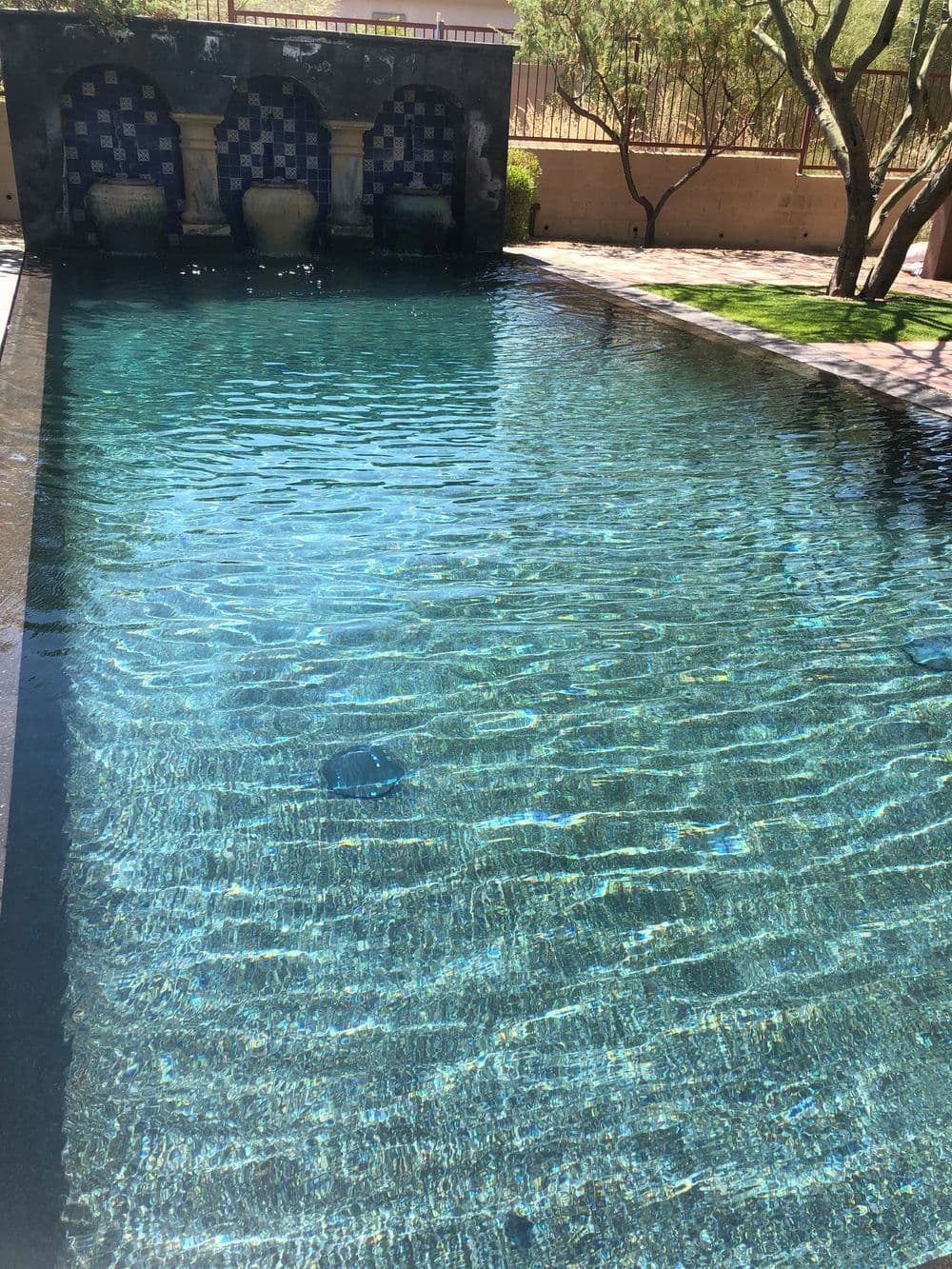 Sparkling blue swimming pool with elegant fountains and lush greenery surrounding the area.